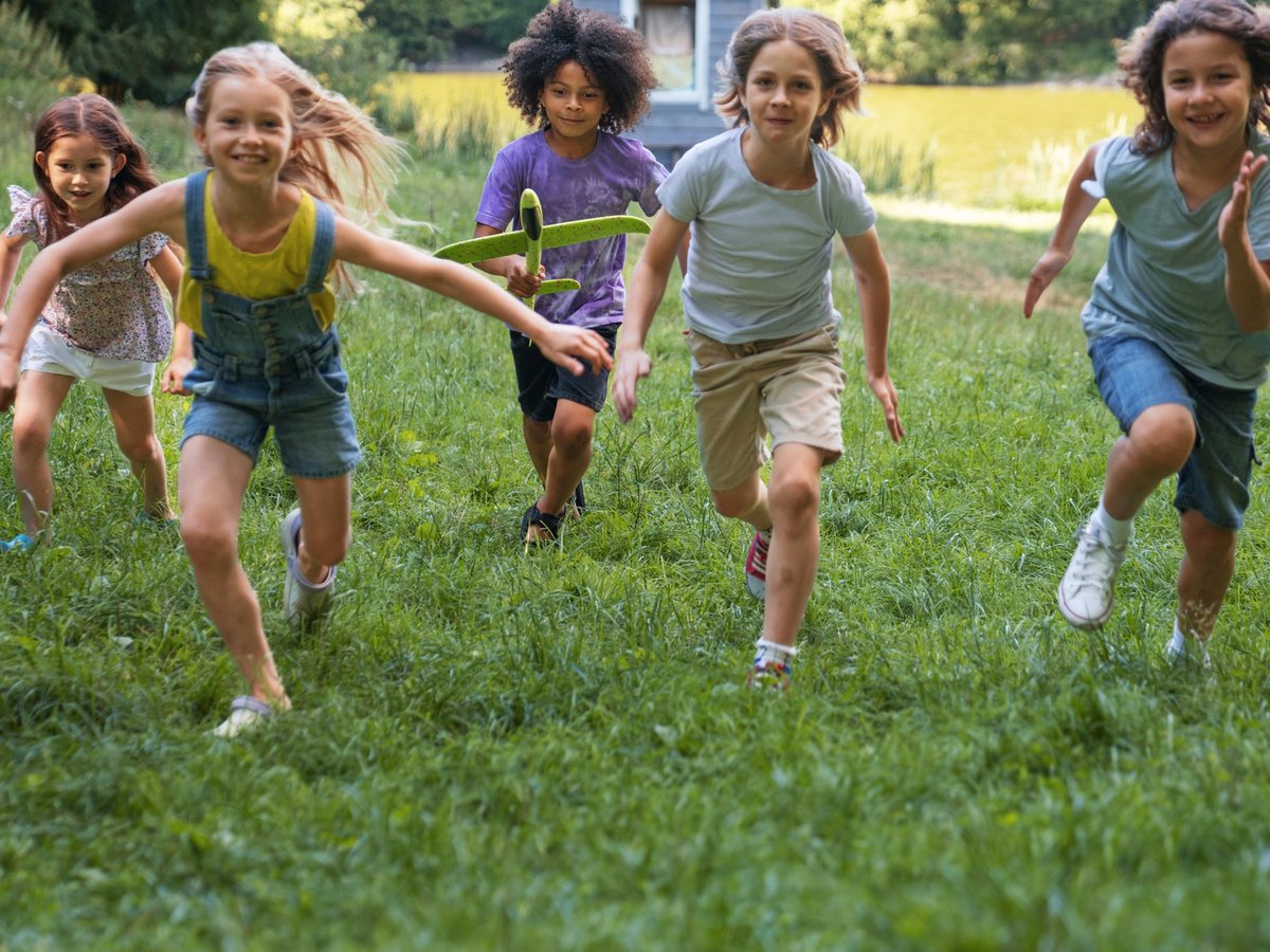 Des enfants courant ensemble dans un champ, un planeur jouet à la main